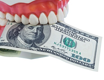 A model denture holding a $100 bill.