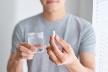 man holding a glass of water and a pill 